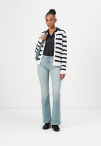 Stripet cardigan i krem og marineblå, ribbet tekstur. Kombinert med lyseblå, vide jeans, supplert med svarte sko og en grå skulderveske.