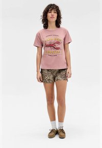 Pink graphic t-shirt featuring a lobster design, paired with brown leopard print shorts. Model wears brown shoes and white socks.