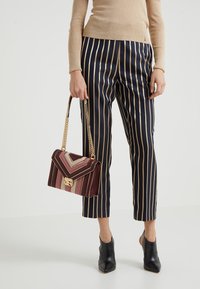 Pantalones a rayas en azul marino y dorado combinados con un bolso de chevrones multicolor con una cadena dorada, complementados por botas de tobillo negras con tacón.