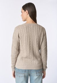 Maglione beige a maglia cable con polsini e orlo a costine. Presenta motivi a cavo verticali e una scollatura arrotondata, realizzato in un morbido tessuto testurizzato.