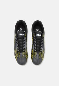 Chaussures de sport noires et grises avec des accents jaunes, présentant un dessus texturé, des lacets ronds et un logo visible sur la languette.