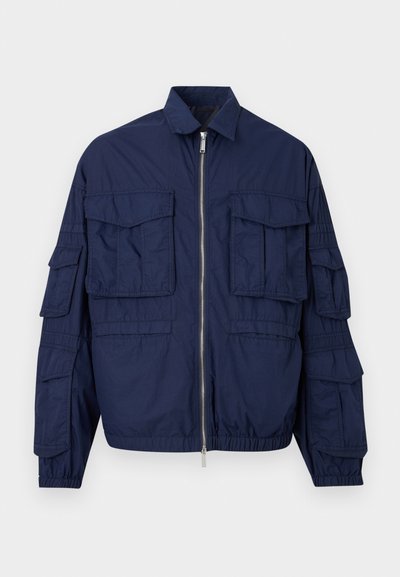 Μπουφάν σε ναυτικό μπλε με φερμουάρ, πολλαπλές τσέπες με καπάκια στο στήθος και στα μανίκια, ελαστικές μανσέτες και γιακά που μοιάζει με πουκάμισο.