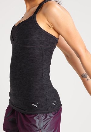 Femme étirant les bras vers l'arrière, portant un débardeur Puma noir et un short de sport violet, avec un petit tatouage d'arbre sur son poignet.