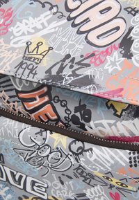 Plecak w wielokolorowy wzór graffiti z szarym tłem, zdobiony różnymi naklejkami i tekstami. Posiada ciemny zamek błyskawiczny i szwy.