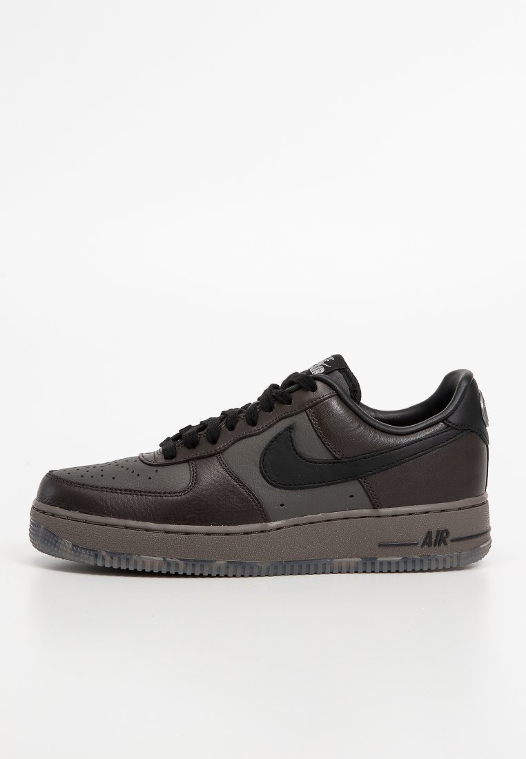 Zapatilla de cuero negra y gris con punta redondeada, vampiro perforado, logo Swoosh negro y suela de goma texturizada que presenta la marca "AIR".