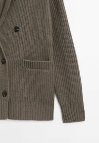 Cardigan marron en maille boutonné avec côtes texturées et poche avant en bas à gauche sur un fond uni.