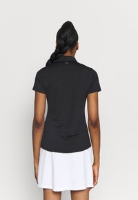 Czarna koszulka polo z krótkim rękawem i kołnierzykiem, zestawiona z białą spódnicą. Tkanina wydaje się gładka i dopasowana w talii.