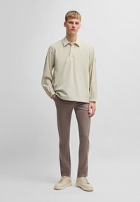 Polo à manches longues beige avec trois boutons, associé à un pantalon slim coupe claire et des baskets beiges. Tissu lisse, coupe décontractée.