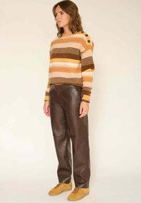 Pull rayé en tricot dans des tons chauds avec des accents de boutons, associé à un pantalon en cuir marron et des baskets moutarde avec des rayures.