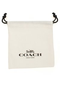Bolsa de tela blanca con cordón negro y el logo "COACH NEW YORK", presentando un diseño decorativo de carruaje y caballo.