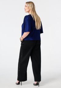 Blauw metallic kort mouwtopje gecombineerd met zwarte broek met wijde pijpen en een zijwaarts paillettenaccent, en hoge hakken.