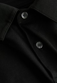 Gros plan sur le col d'une chemise noire avec deux boutons noirs attachés sur un tissu texturé.