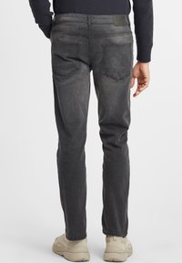Tumedad hallid teksad, millel on slim fit, kahe tagataskuga ja nahast lapi detailiga vöökohal. Materjalil on kulunud tekstuur.