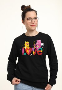 Felpa nera con un design grafico colorato che presenta due orsi stilizzati, cuori e la parola "Amore" in lettere vivaci.