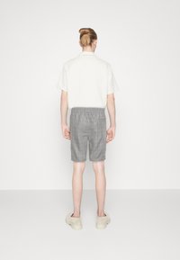 Camisa blanca de manga corta, pantalones cortos de cuadros grises a medida y zapatos ligeros de tipo slip-on. Diseño simple, ajuste relajado y cinturilla elástica en los pantalones cortos.