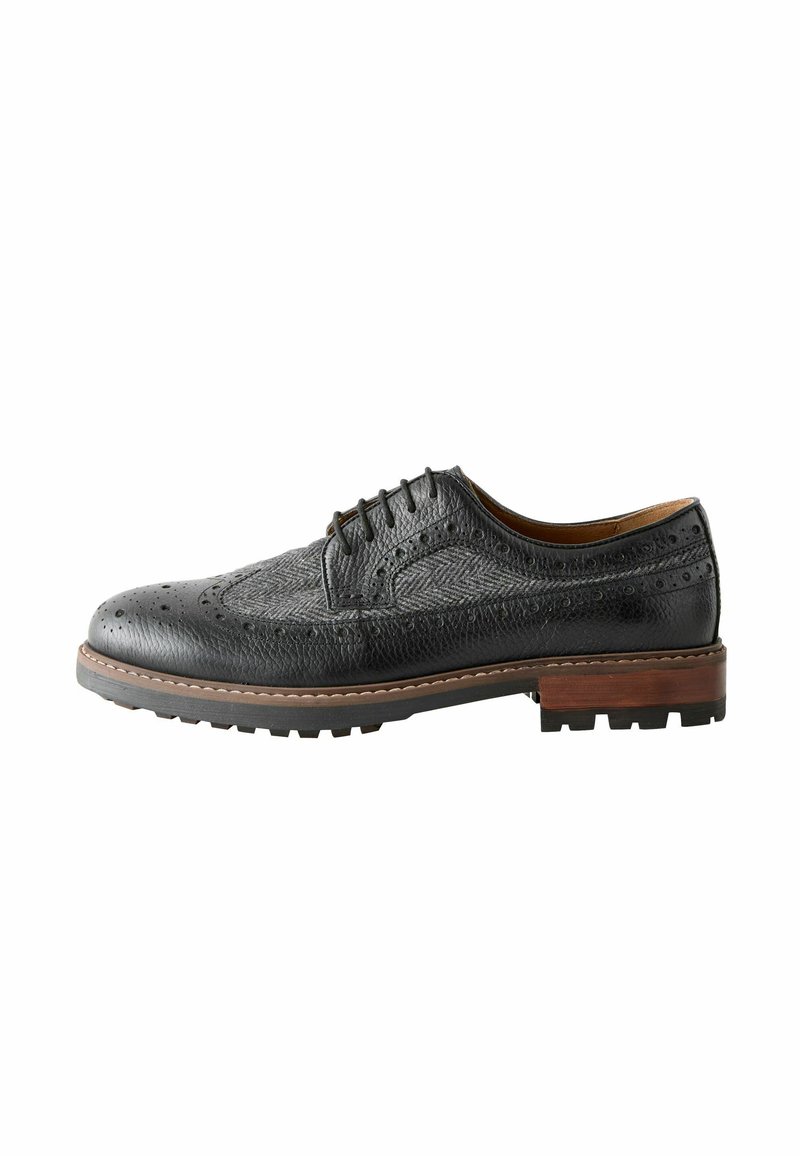 Black leather dress shoe with textured surface, brogue detailing, and a brown wooden midsole. Features a rugged rubber sole for grip.