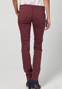 Jeans ajustados burdeos hechos de material de algodón elástico; cuentan con dos bolsillos traseros y un pequeño parche con logo en la cintura.