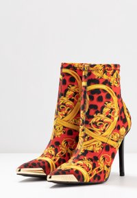 Stivali ankle con stampa animale rossa e nera, ornati da disegni dorati, punta affusolata e tacco a stiletto alto. Accento dorato sulla punta.