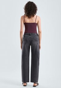 Zwarte denim wijde broek met een hoge taille, voorzien van achterzakken en een rafelige zoom. Gepaard met een bordeauxrode aansluitende tanktop.