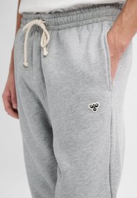 Grijze katoenen joggingbroek met een elastische tailleband en een trekkoord, met zijzakken en een kleine geborduurde bij als accent op de dij.
