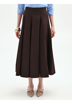 Donna con gonna midi marrone a linea A, camicia azzurra con maniche risvoltate, bracciale rigido d'oro al polso sinistro e tacchi intrecciati appuntiti.