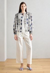 Giacca leggera stampata con maniche a sbuffo, motivo blu navy e bianco. Abbinata a pantaloni a gamba larga in maglia off-white e sandali con tacco azzurri.