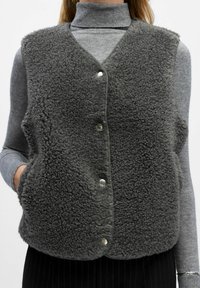 Grå fleece vest med en tekstureret overflade, med V-hals, trykknaplukning og sidelommer, båret over en grå turtleneck.