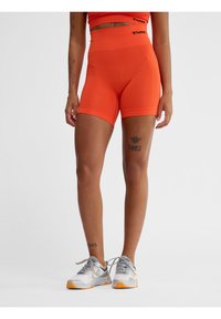 Felgekleurde oranje sportshorts met een hoge tailleband, gemaakt van rekbaar materiaal, gecombineerd met witte en grijze sneakers met oranje accenten.