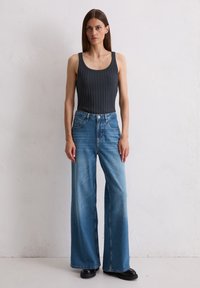 Grijze geribbelde tanktop gecombineerd met een wijde blauwe denim jeans. De jeans hebben een vervaagde afwerking en voorzakken, met zwarte schoenen.