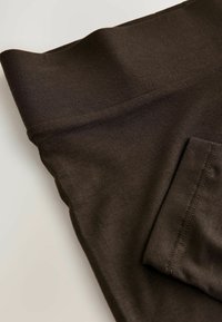 Tmavohnedé legíny vyrobené z mäkkého a elastického materiálu. Majú vysoký pás a prehnuté manžety. Obsahujú malú bočnú vrecko.