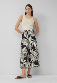 Crème tanktop met geribbelde textuur, gecombineerd met zwarte wijde broek met een wit bladprintontwerp. Zwarte schuifsandalen.