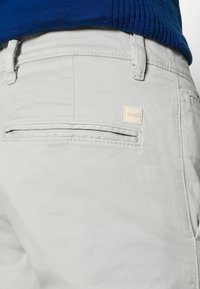 Světle šedé bavlněné kalhoty s slim fit, s jednou zadní kapsou, jemným šitím a malým hnědým logem BOSS na pásku.