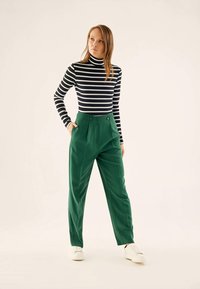 Black and white striped turtleneck, paired with high-waisted green trousers featuring front pleats and button details, completed with white sneakers.