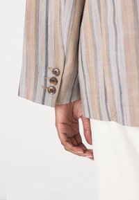 Stripet blazer i brune, beige og blåtoner; har tre brune knapper på mansjetten og et strukturert stoff. Slim fit med skreddersydde detaljer.