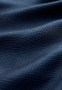 Tumesinine kangas tekstureeritud mesilasemaustrilaadse mustriga ja pehmete voltidega, mis loovad õrnu varje.