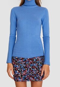 Blauwe coltrui van een zachte gebreide stof, gecombineerd met een minirok met bloemenpatroon en veelkleurige bloemen op een donkere achtergrond.