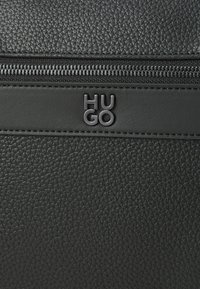 Juoda tekstūruota dirbtinės odos kuprinė su viršutiniu užtrauktuku ir matinio juodo "HUGO" logo žyme. Lygūs akcentai pagerina jos dizainą.