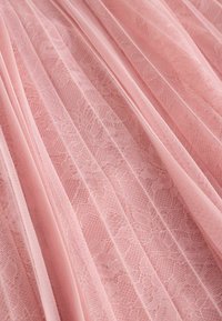 Mīksts rozā krokojums audums ar smalkām ziedu mežģīņu rakstiem un smalku tīklojuma struktūru, sakārtots maigos locījumos.