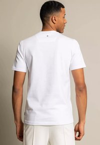 Bia ła koszulka z krótkim rękawem, okrągłym dekoltem, wykonana z gładkiej bawełnianej tkaniny, z małym logo na górze pleców.