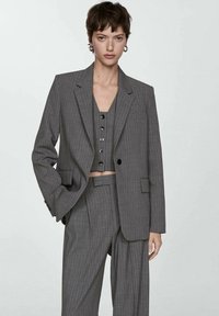 Gray pinstriped suit featuring a loose-fitting blazer, cropped button-up top, and wide-leg trousers, made from lightweight fabric.