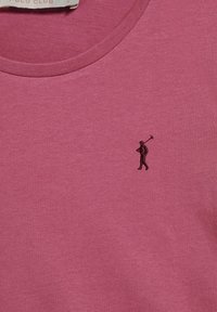 Rosa bomullst-shirt med rund halsringning. Har en liten svart broderad golfspelare-logotyp på vänster bröstområde. Mjuk textur.