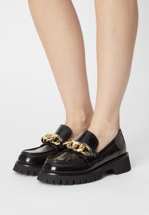 Mocassins en cuir verni noir avec un accent de chaîne dorée épaisse et une semelle noire épaisse. Le design comprend un profil bas et un bout arrondi.