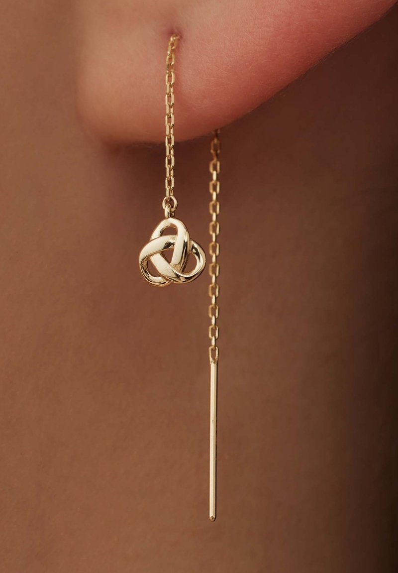 Boucles d'oreilles en chaîne dorée avec un pendentif en forme de nœud et un accent de tige droite et élancée. Fini brillant avec des détails complexes sur le pendentif.
