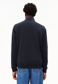 Sudadera de manga larga de color navy con cuello alto, puños y dobladillo acanalados. Tejido suave con una textura lisa, combinado con jeans de color azul claro.