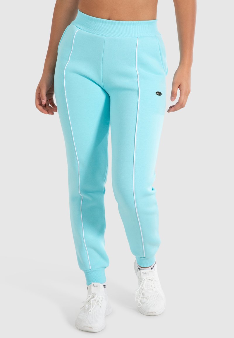 Lichtblauwe joggingsbroek van een zachte katoenmix, met witte zijkanten en een elastische tailleband. Gepaarde met witte sneakers.