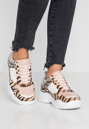 Baskets à imprimé léopard avec mesh rose et accents blancs. Semelle amortissante, empeigne texturée et design à lacets. Portées avec un jean noir effiloché.