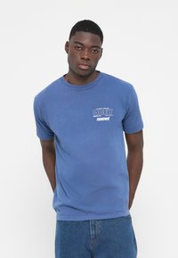 Blue cotton t-shirt with short sleeves and a crew neck. Features a printed "OBEY" logo and text on the left chest. Simple design, relaxed fit.