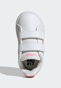 Bílá teniska s růžovými akcenty, vyrobená z hladkého syntetického materiálu. Má dva suché zipy a texturovaný jazyk z látky.