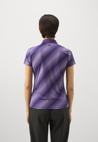 Lilla polo skjorte med korte ermer, med diagonale hvite striper og klassisk krage. Glatt tekstur, designet for trening.