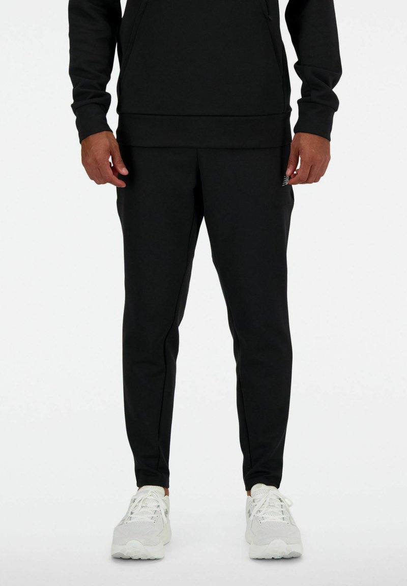 Completo felpa nera e pantaloni, realizzato in un materiale morbido. Presenta una vestibilità morbida, polsini a costine e un dettaglio del logo sulla gamba del pantalone. Sneakers bianche.
